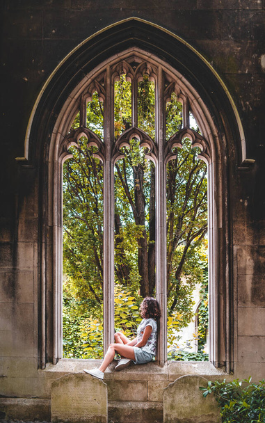 Junge Frau sitzt am Kirchenfenster in St. Dunstan im Osten Londons, England, Großbritannien - Foto, Bild