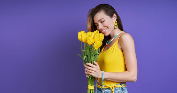 Attractive young woman smelling a bunch of flowers against purple background - Fotoğraf, Görsel