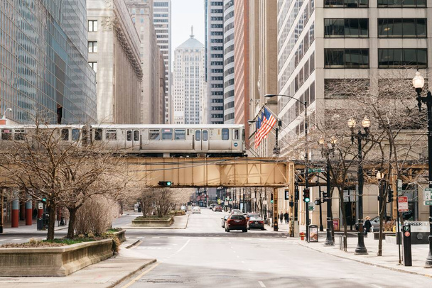 A street view in Chicago of train passing between modern buildings over cars in the street - Foto, Imagem