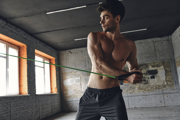 Concentrated young man exercising with elastic resistance band in gym - Foto, afbeelding