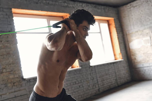 Confident young man exercising with elastic resistance band in gym - Photo, image