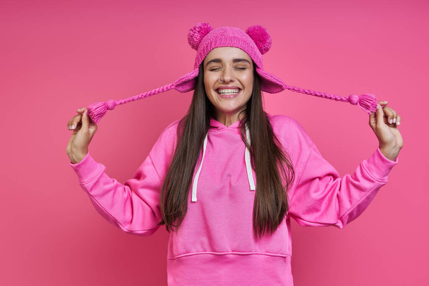 Happy young woman in hooded shirt stretching her funky hat against pink background - Foto, imagen