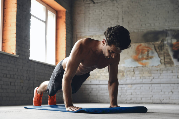 Concentrated young man doing push-up exercises in gym - Foto, Imagen