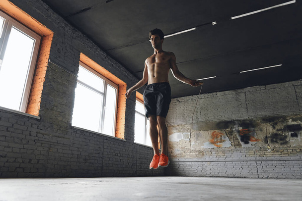 Full length of confident young man jumping with rope in gym - Foto, Imagem