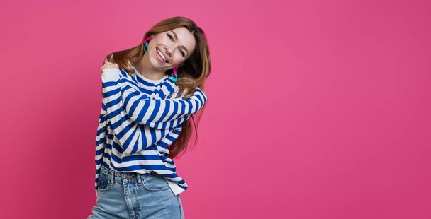 Happy young woman hugging self and smiling while standing against colored background - Fotoğraf, Görsel