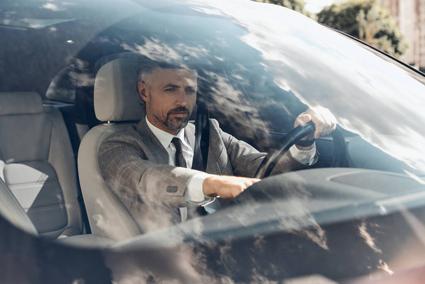 Confident mature man in formalwear using control panel while sitting on the front seat of a car - Foto, Imagen