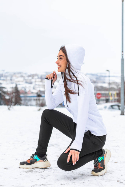 Портрет молодої задоволеної усміхненої і зосередженої спортивної активної дівчини, яка зігріває в зимовому спортивному одязі засніжену природу вранці
. - Фото, зображення