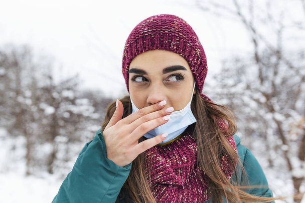 Young woman touching her nose with dirty hand. Avoid touching your nose. Woman wearing face mask rubbing her nose outdoor.Don't touch your face, stop spreading Coronavirus - Photo, image