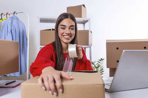 Young woman, owener of small business packing product in boxes, preparing it for delivery. Women packing package with her products that she selling online - Foto, Imagen
