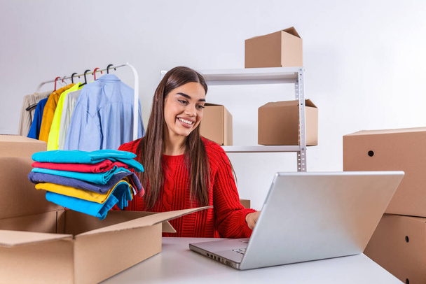 Woman packing item that she sells online. Working woman at online shop. She wearing casual clothing and checking on laptop address of customer and package information. small owner business - Foto, imagen