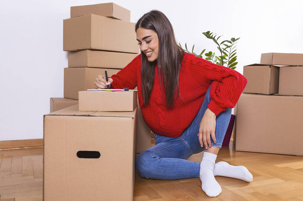 Молода жінка рухає нове місце і концепцію ремонту щаслива молода жінка з багатьма картонними коробками, сидячи на підлозі вдома
 - Фото, зображення