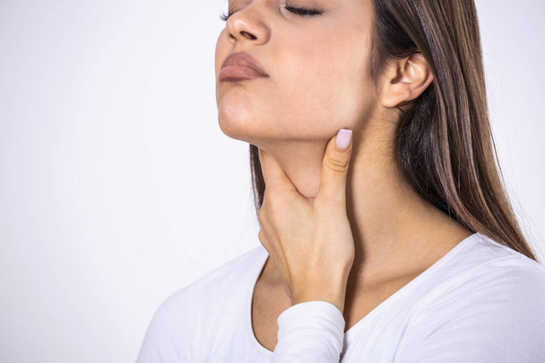 Young beautiful woman suffering from pain in throat, touching inflamed zone on her neck, cropped, empty space, sore throat - Фото, изображение