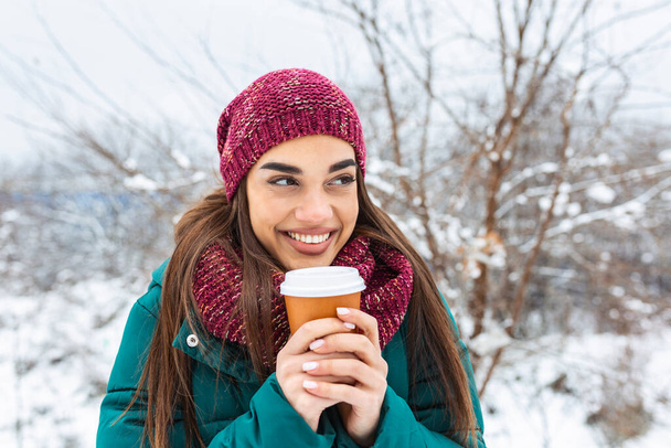 Onnellinen nuori nainen kertakäyttöinen kuppi kahvia tai teetä yllään lämpimät vaatteet. Kaunis tyttö tilalla kertakäyttöinen kuppi, seisoo ulkona talvella - Valokuva, kuva