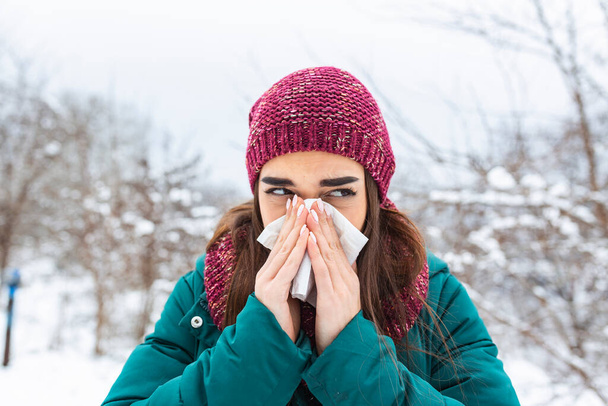 Nuori nainen puhaltaa nenäliinaan kylmänä talvena luminen vuori taustalla. Muotokuva naisesta, jolla on nenäliina käsissään. Tytöllä on flunssa ja nenän vuotaminen - Valokuva, kuva