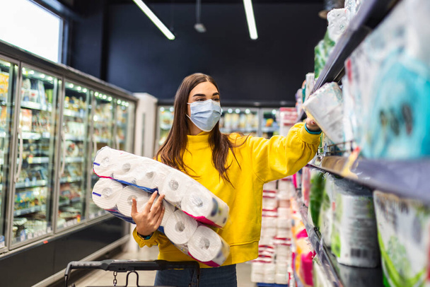 Kobieta z maską higieniczną na zakupy papieru toaletowego z powodu zakupu paniki i gromadzenia produktów podczas epidemii wirusów.Produkty higieniczne niedobór zapasów zdjęcie - Zdjęcie, obraz