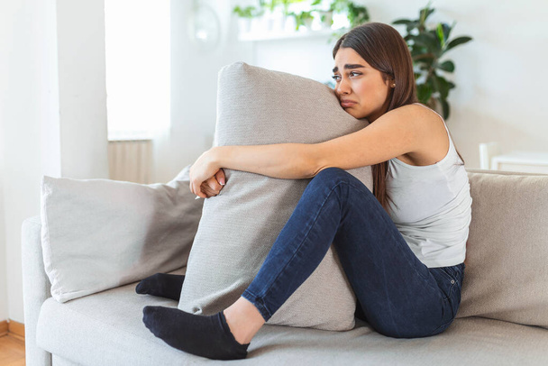 Difficult times. Portrait of a cheerless sad caucasian woman holding her hands crossed and hugging big pillow while thinking about her problems. Stock photo - Photo, Image