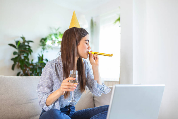 Copy space shot of a cheerful young woman having a birthday celebration event with a friend over a video call. She is making a celebratory toast with a glass of white wine towards laptop camera. - 写真・画像