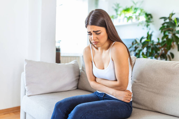Woman in painful expression holding hands against belly suffering menstrual period pain, lying sad on home bed, having tummy cramp in female health concept - Zdjęcie, obraz