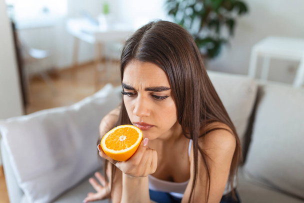 Больная женщина, пытающаяся почувствовать запах полусвежего апельсина, имеет симптомы Ковид-19, коронная вирусная инфекция - потеря запаха и вкуса. Один из основных признаков заболевания. - Фото, изображение