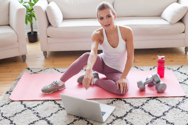 Mujer joven flexible haciendo ejercicio en casa, utilizando el ordenador portátil  - Foto, imagen