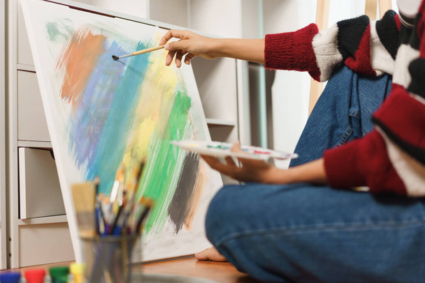 The art concept, Asian female artist sit on the floor and using paint brush to painting on canvas. - Photo, Image