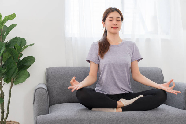 Yoga exercise concept, Young Asian woman doing yoga exercise in lotus pose on couch in living room. - Zdjęcie, obraz
