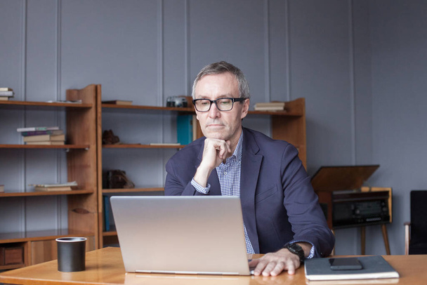 Концентрований старший бізнесмен використовує ноутбук в офісі
 - Фото, зображення