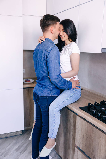 Een romantisch stel knuffelt een meisje aan de keukentafel, een man kust een vrouw. - Foto, afbeelding