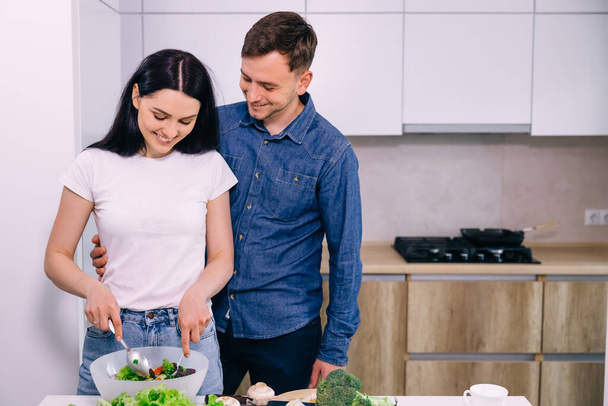 Young couple preparing vegetarian food. They have fun in the kitchen and prepare salad. - Foto, Bild