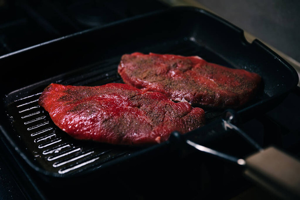 Primer plano de sartén de metal con trozo de carne fresca y aceite caliente de pie en la superficie de la estufa moderna
 - Foto, Imagen
