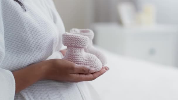 Happiness of childbirth. Close up shot of unrecognizable pregnant woman holding cute tiny knitted booties, side view, home interior, slow motion, empty space - Imágenes, Vídeo
