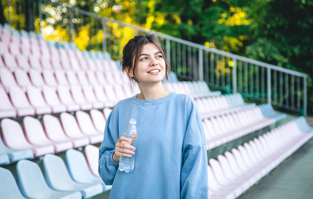 Attractive cheerful young woman sportswoman drinks water after training outdoors in the stadium. - Foto, Imagem