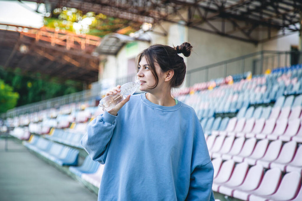 Attractive cheerful young woman sportswoman drinks water after training outdoors in the stadium. - Foto, imagen