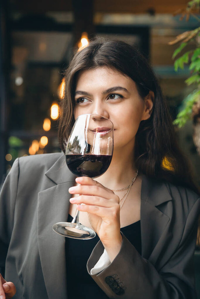 Pencerenin yanındaki restoranda elinde bir bardak kırmızı şarapla çekici bir genç kadın.. - Fotoğraf, Görsel