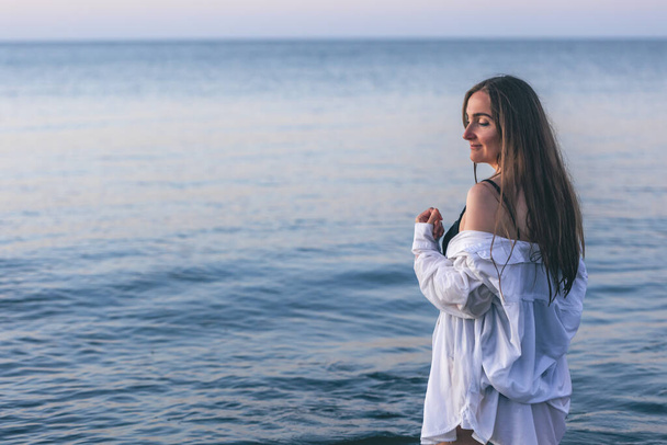 A woman in a bathing suit and a white shirt in the sea at sunset, copy space. - Foto, imagen