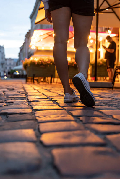 Womens feet stand on a paving stone road in the evening ancient city. - Photo, image