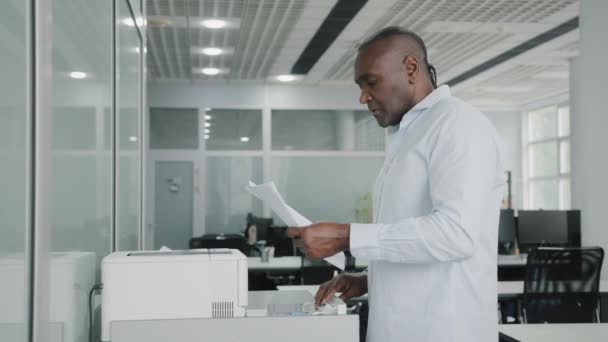 Afrikaanse amerikaanse senior volwassen zakenman vult papier in printer kantoorapparatuur elektronische machine leveren van blanco pagina 's te lade drukken knoppen op display afdrukken documenten scannen maken kopieën - Video
