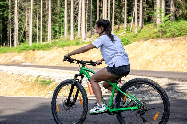 Athletic young woman rides a bike in a mountainous area in the forest, copy space. - Фото, изображение