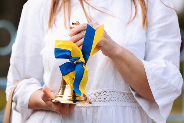 cropped photo of female hands holding school bell with a blue yellow bow - a symbol of the beginning of the school year or graduation in Ukraine. Concept of education. Back to school - Fotó, kép