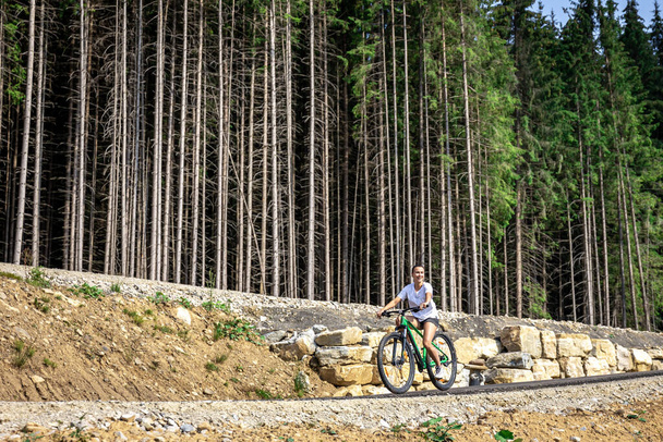 Atletik genç kadın ormanın dağlık bir bölgesinde bisiklet sürüyor, uzayı taklit ediyor.. - Fotoğraf, Görsel