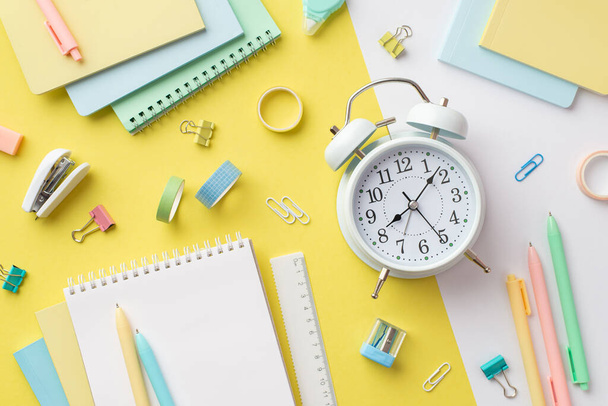 School accessories concept. Top view photo of alarm clock colorful notepads sharpener ruler pens binder clips adhesive tape and stapler on bicolor yellow and white background - Foto, Imagem