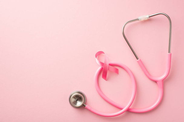 Breast cancer prevention concept. Top view photo of pink ribbon over stethoscope on isolated pastel pink background with empty space - Foto, immagini