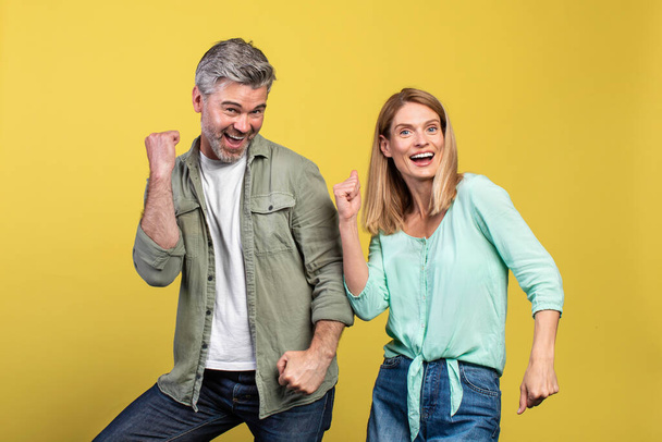 Portarit of joyful middle aged caucasian spouses dancing and fooling around, enjoying favorite music together on yellow studio background - Fotografie, Obrázek
