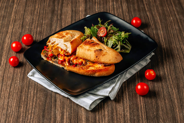 cheese steak sandwich with meat, vegetables, cheese and sauce served in the black tray on a dark wooden table. American street food top view - Φωτογραφία, εικόνα