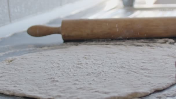 Cook rolls out the dough for pizza with a rolling pin. The cook rolls out the dough, chef is baking, bakery products, making the dough - Materiał filmowy, wideo
