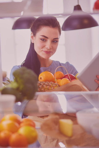 Smiling woman taking a fresh fruit out of the fridge, healthy food concept. - Foto, afbeelding
