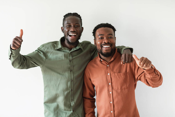 Two Cheerful African American Guys Gesturing Thumbs Up Approving Offer Smiling To Camera Standing Over White Studio Background. We Like It Concept. Selective Focus - Fotografie, Obrázek
