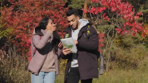 Happy young couple in love hiking tourists backpacking outdoors talking discussing arguing guy looks at paper map in search of correct route girl uses mobile application for geolocation on smartphone - Imágenes, Vídeo