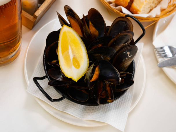 Pile of steamed mussels with lemon wedge in metal serving pan. Popular seafood beer snack - Fotoğraf, Görsel