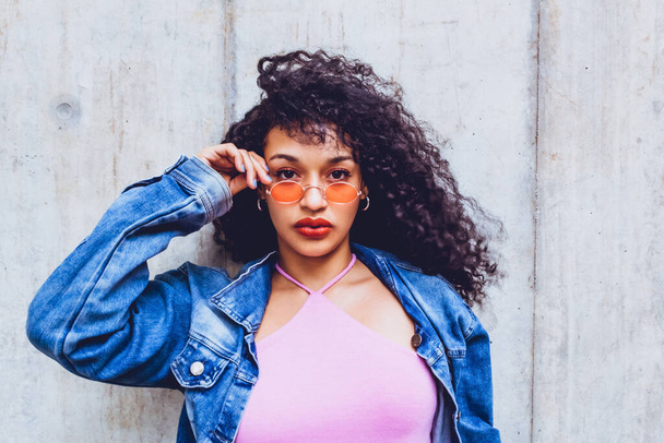 closeup portrait of teen woman wearing orange glasses and blue jacket posing in city trendy looking on isolated gray background, generation z woman in city, urban concept. - Zdjęcie, obraz